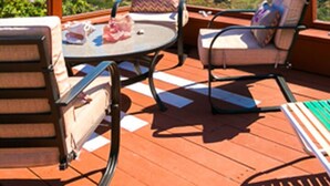 Eine Terrasse mit Gartenmöbeln, darunter ein Tisch und Stühle, mit Blick auf eine malerische Meereslandschaft und die Küste.