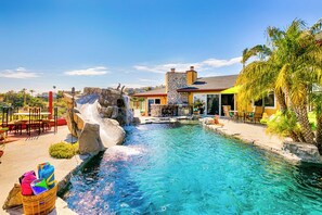 Una piscina con una cascada, mobiliario exterior y un edificio de piedra con techo amarillo.