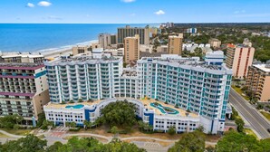 A large hotel with multiple floors, a central courtyard with a swimming pool, and a view of the ocean.