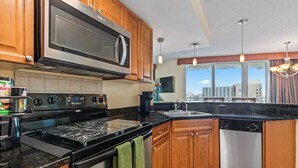 A modern kitchen with wooden cabinets, a stainless steel microwave, a black countertop, and a dishwasher.