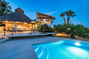 A modern resort with a swimming pool, outdoor seating, and a thatched-roof structure.