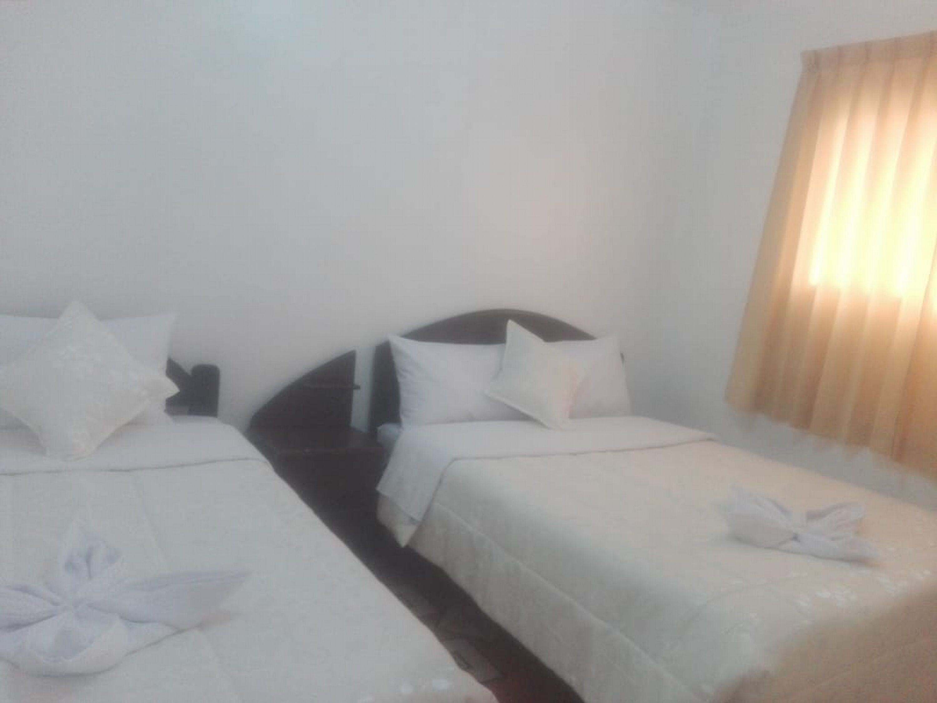 A hotel room with two single beds, each with white bedding and pillows, and a headboard.