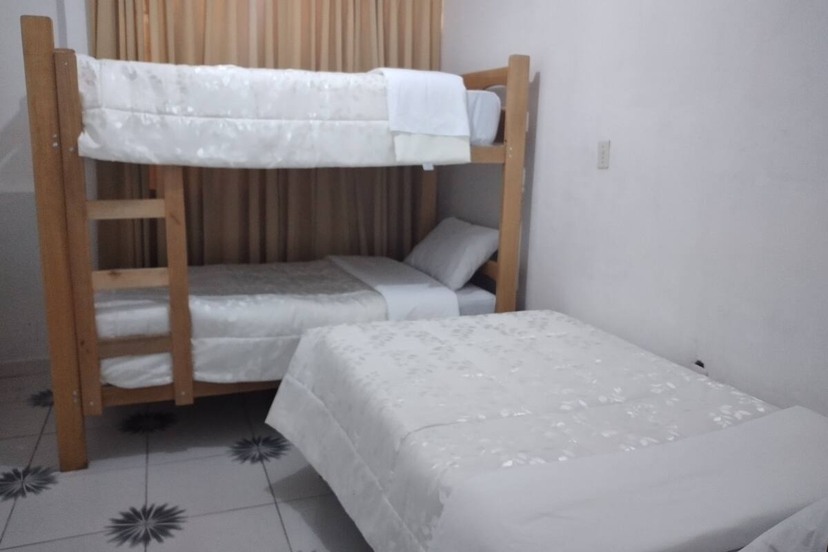 A bunk bed with a ladder, a single bed, and a curtain in the background.