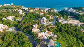 An aerial view of a coastal town with a mix of residential and commercial buildings, a prominent hotel with a swimming pool, and a clear view of the ocean. - Vista Hermosa (Santa María Huatulco)