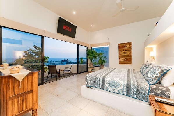 Un dormitorio con una cama grande, televisor, balcón con vistas y un escritorio de madera.