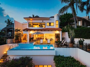 Una casa moderna de dos pisos con piscina, mobiliario exterior y un jardín bien cuidado.