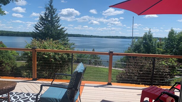 A deck with a view of a lake, a red umbrella, and outdoor furniture. - All Year Lakefront Getaway in a private guest rm & indoor heated pool !! (Westport)