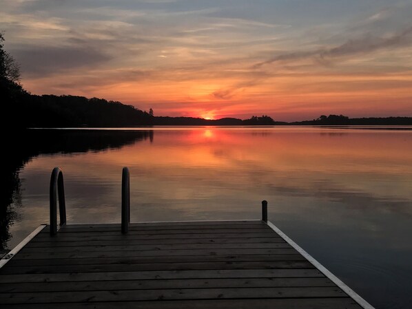 Une jetée en bois s’étendant sur une étendue d’eau calme, avec un coucher de soleil en arrière-plan.
