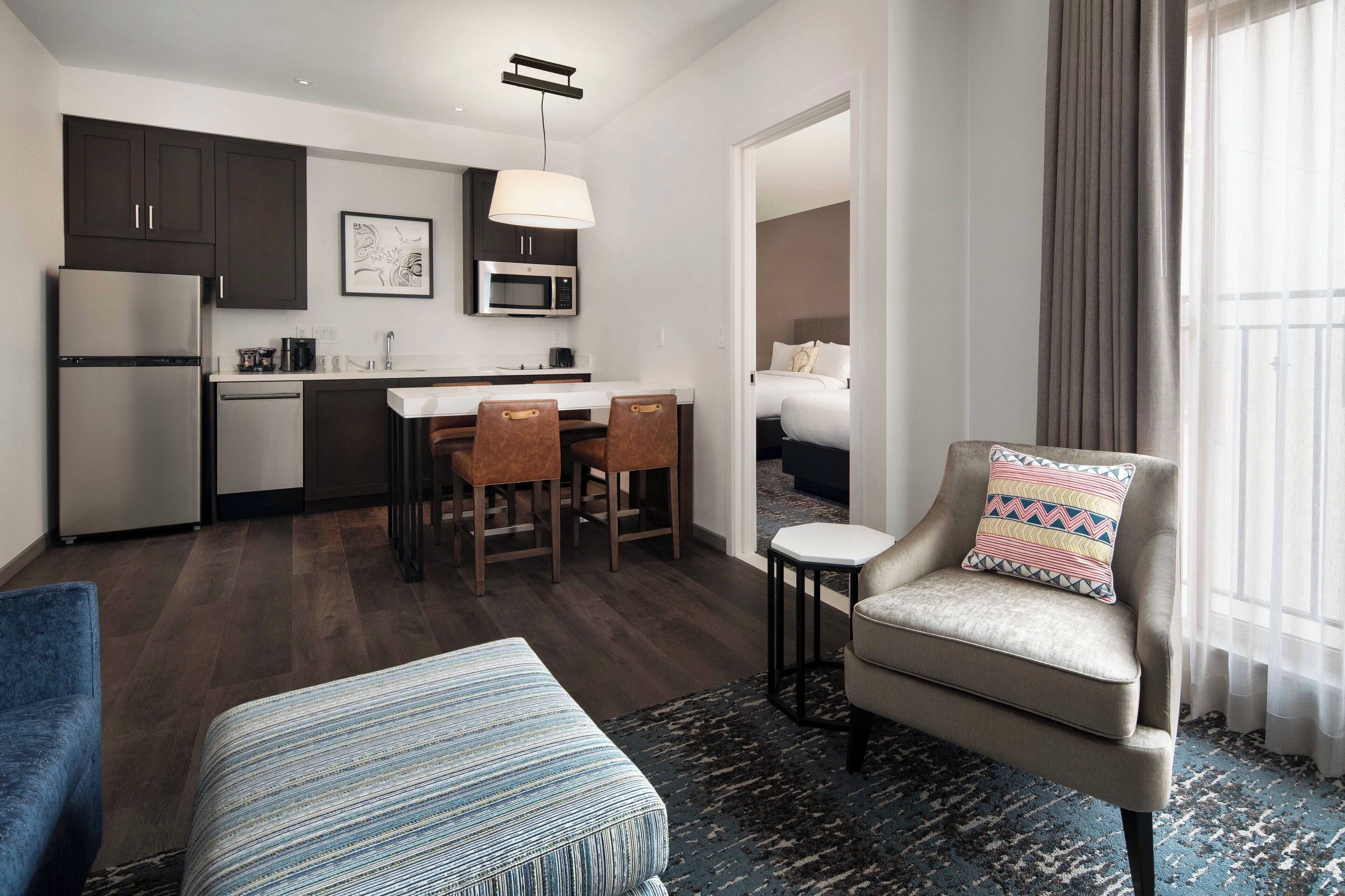 A compact hotel room with a kitchenette, a dining area, a sofa, and a view of the outside.