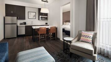 A compact hotel room with a kitchenette, a dining area, a sofa, and a view of the outside.