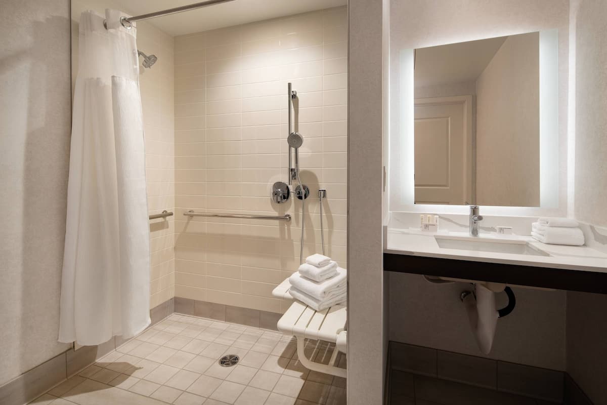 Un baño moderno con ducha a nivel, inodoro con barra de apoyo y lavamanos con espejo.