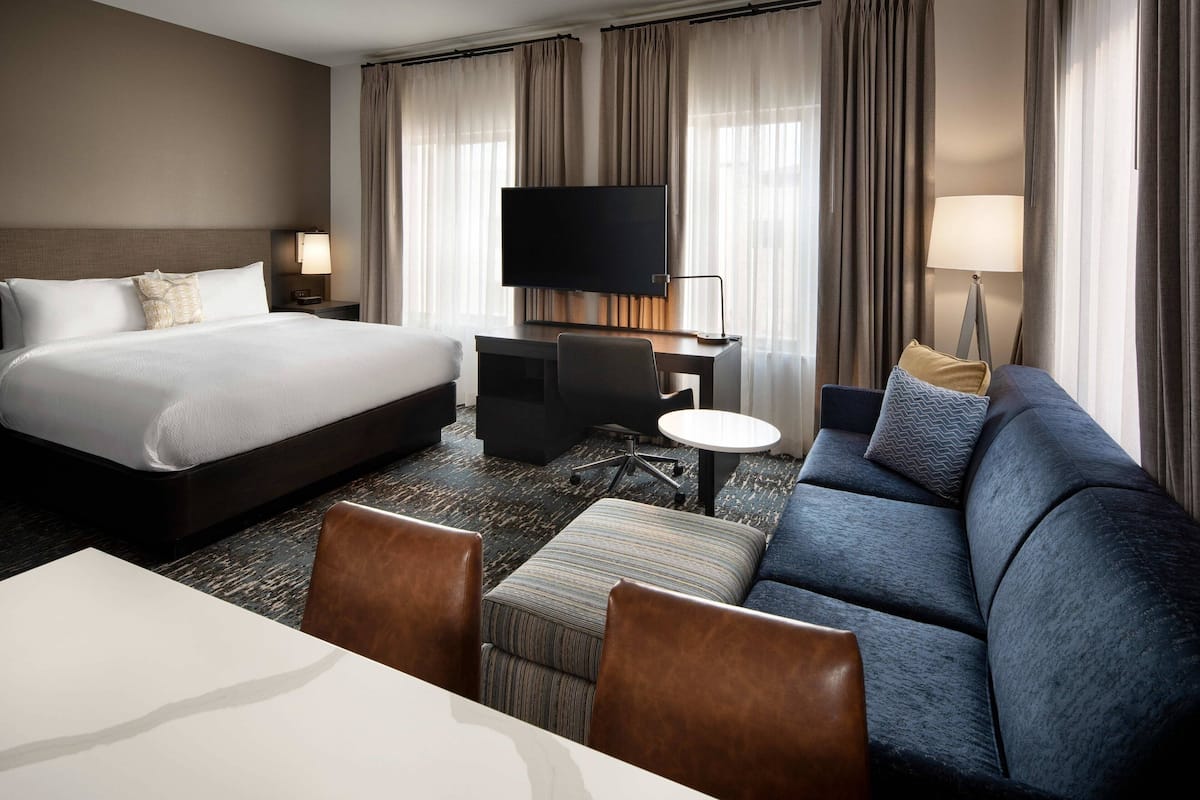 Habitación de hotel con una cama grande, un sofá, un escritorio con televisor y una mesita.