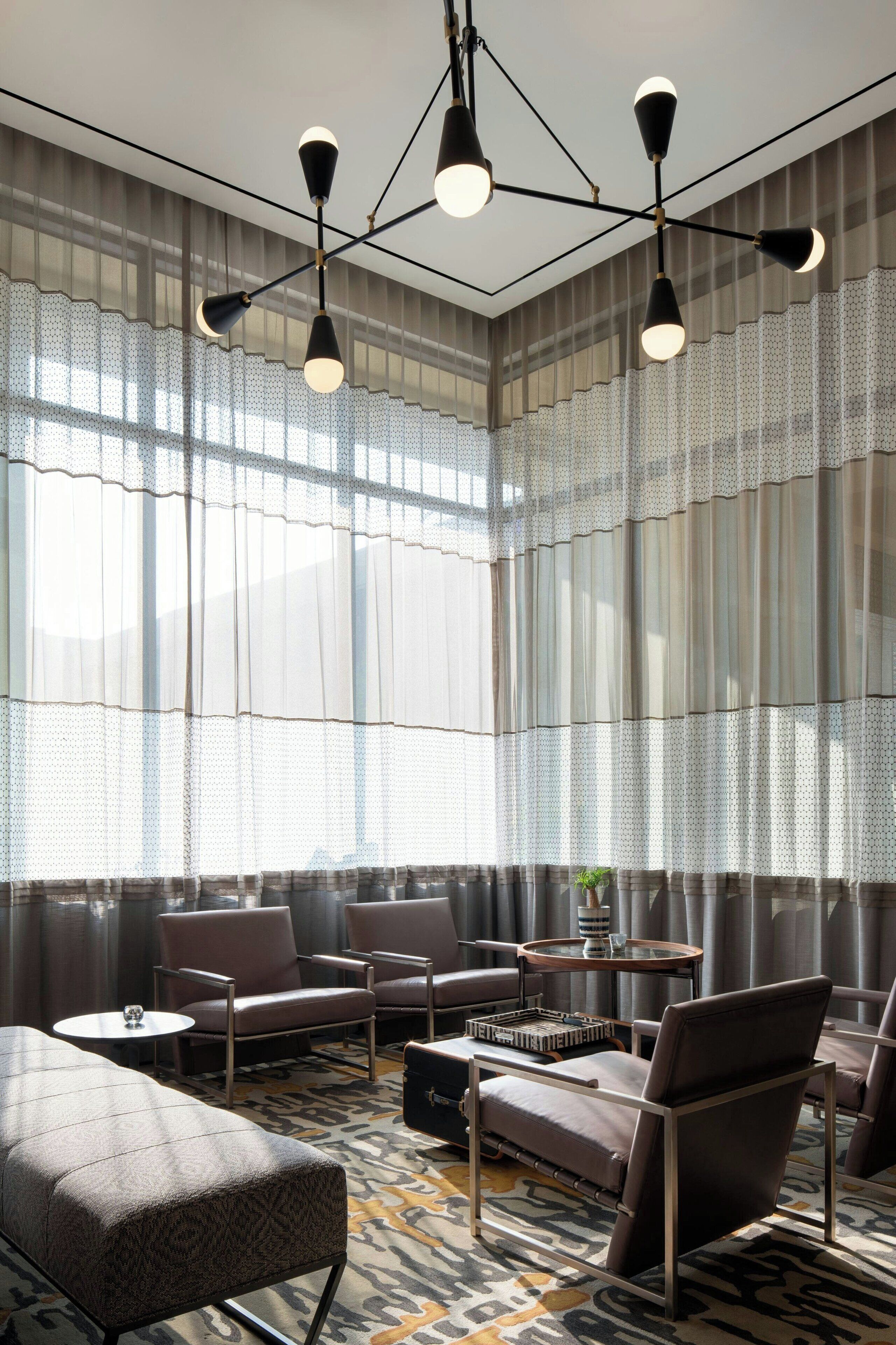 A modern hotel lobby with a large seating area, a patterned carpet, and a chandelier.