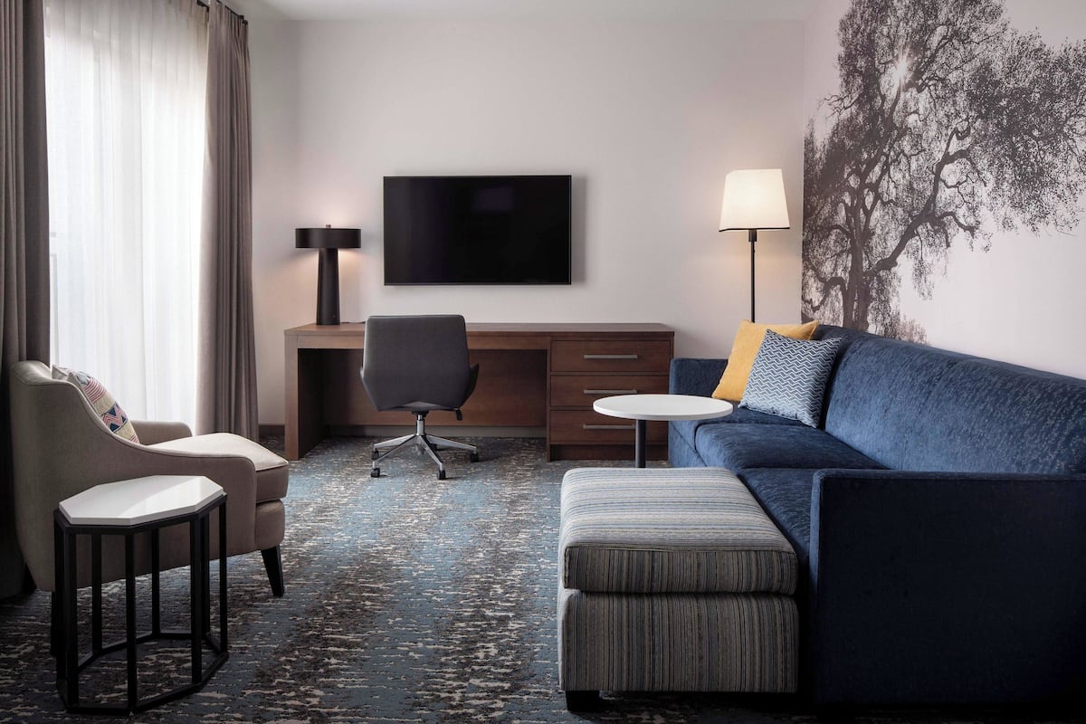 Habitación de hotel con sofá, sillón, escritorio y televisor.