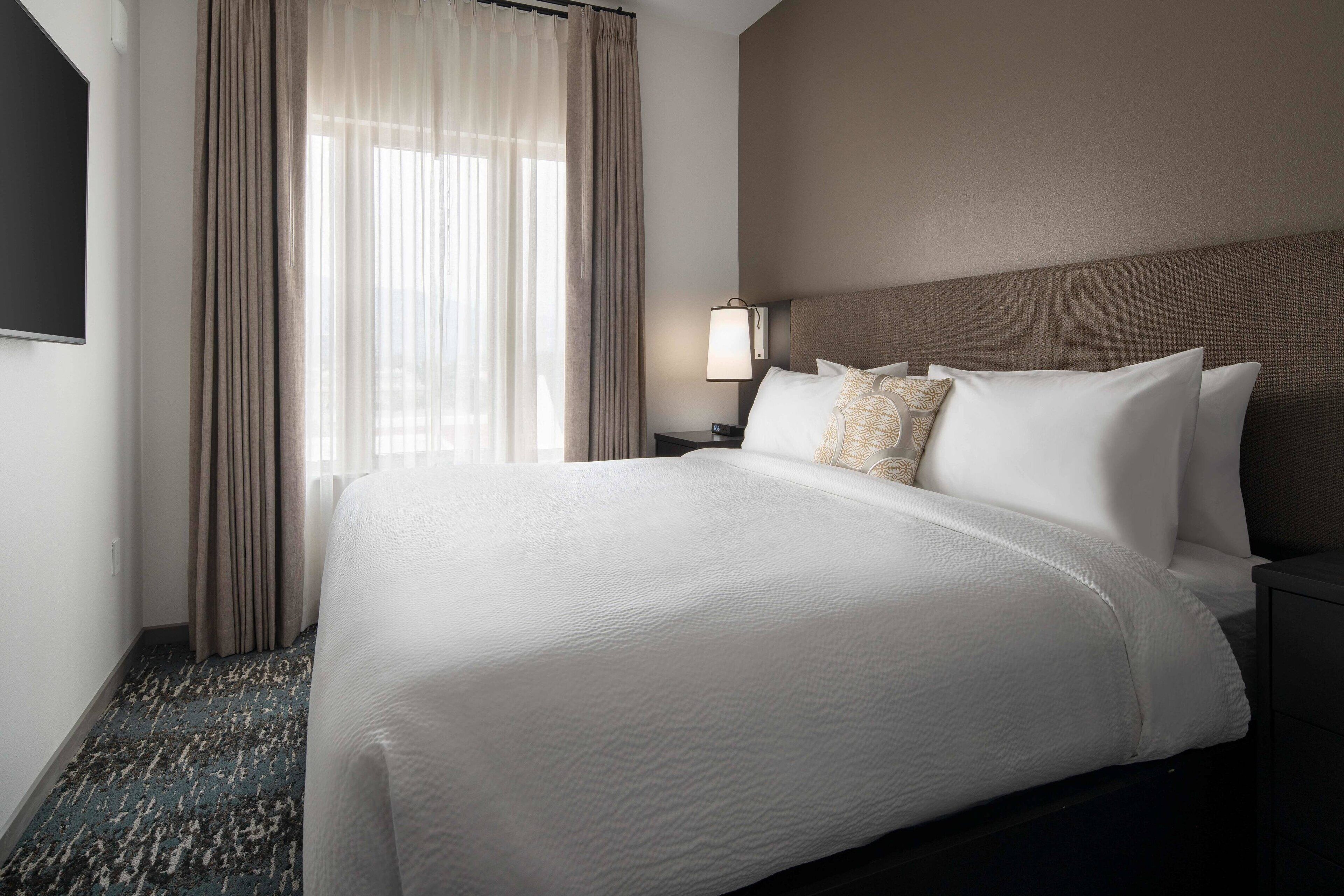 A hotel room with a large bed, a nightstand with a lamp, and a window with curtains.