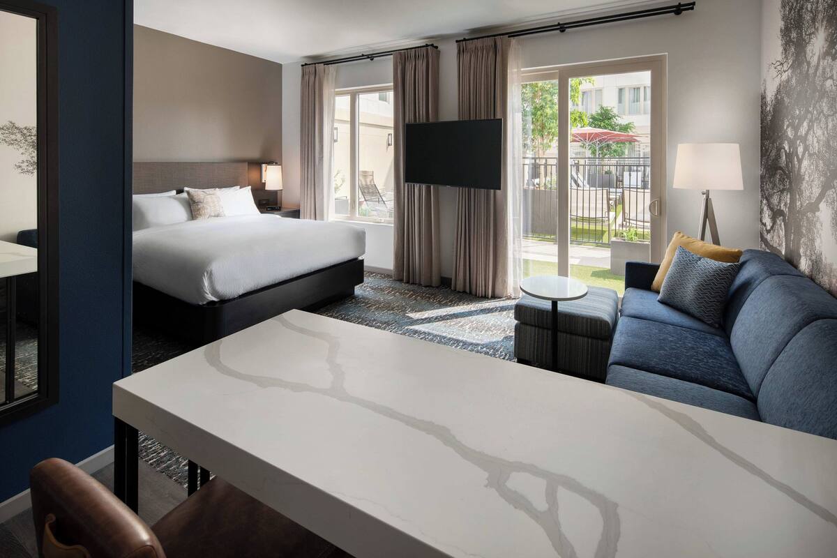 Una habitación de hotel con cama, sofá, televisión y mesa de comedor.