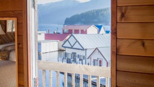 A wooden cabin with a balcony overlooking a lake and buildings.