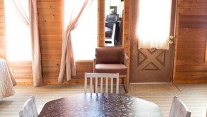 A wooden cabin interior with a round dining table, white chairs, and a door leading to another room.
