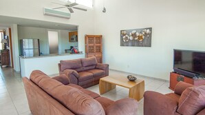 Ein Wohnzimmer mit braunen Sofas, einem Holztisch, einem Fernseher und einer Küche im Hintergrund.