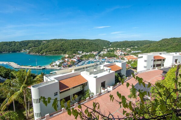 A coastal town with a marina, white buildings with red roofs, and lush green hills in the background. - Cruz Del Mar M302 (Santa María Huatulco)