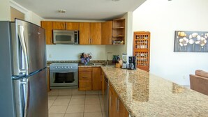 Eine Küche mit Kühlschrank, Herd, Mikrowelle, einer Arbeitsplatte aus Granit, Holzschränken und einer Kaffeemaschine.