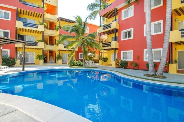 A swimming pool surrounded by colorful buildings with balconies and palm trees. - Hacienda Real (Santa María Huatulco)