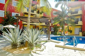 A pool area with a clear blue pool, surrounded by palm trees and a covered seating area. - Hacienda Real (Santa María Huatulco)