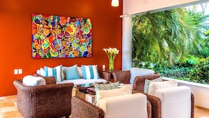 Una sala de estar moderna con un cuadro grande de una mariposa colorida, muebles de mimbre y vistas a exuberante vegetación.