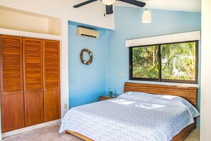 A bedroom with a bed, a wardrobe, an air conditioning unit, a window with a view of greenery, and a ceiling fan. - Villa Rebeca (Santa María Huatulco)