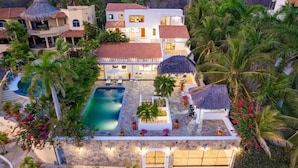 Un gran resort de varios pisos con piscina, palmeras y una estructura de techo de paja.