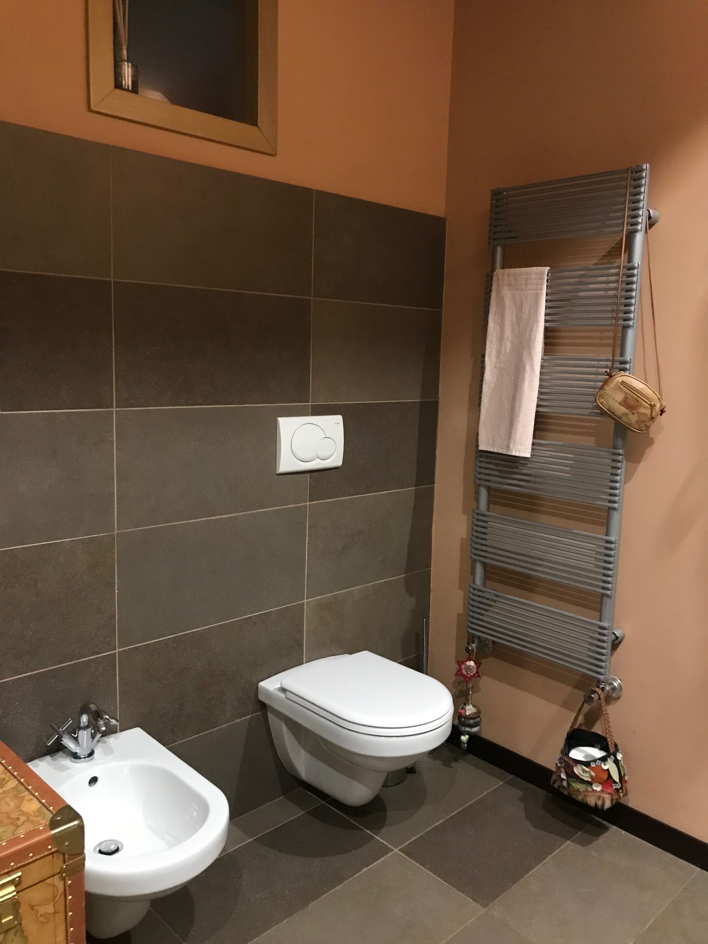 A bathroom with a bidet, toilet, and sink. There is a towel rack with a towel and a handbag.