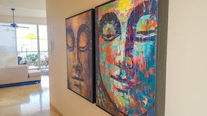 A hallway with two large abstract paintings on the wall, a ceiling fan, and a view of a balcony with plants and a yellow umbrella.