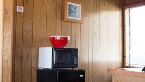 A compact kitchen with wooden walls, a black refrigerator, a microwave, and a small window.