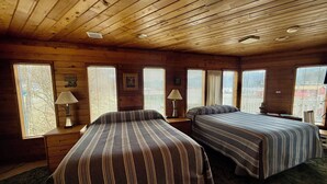 A cabin with two beds, wooden walls, and large windows.