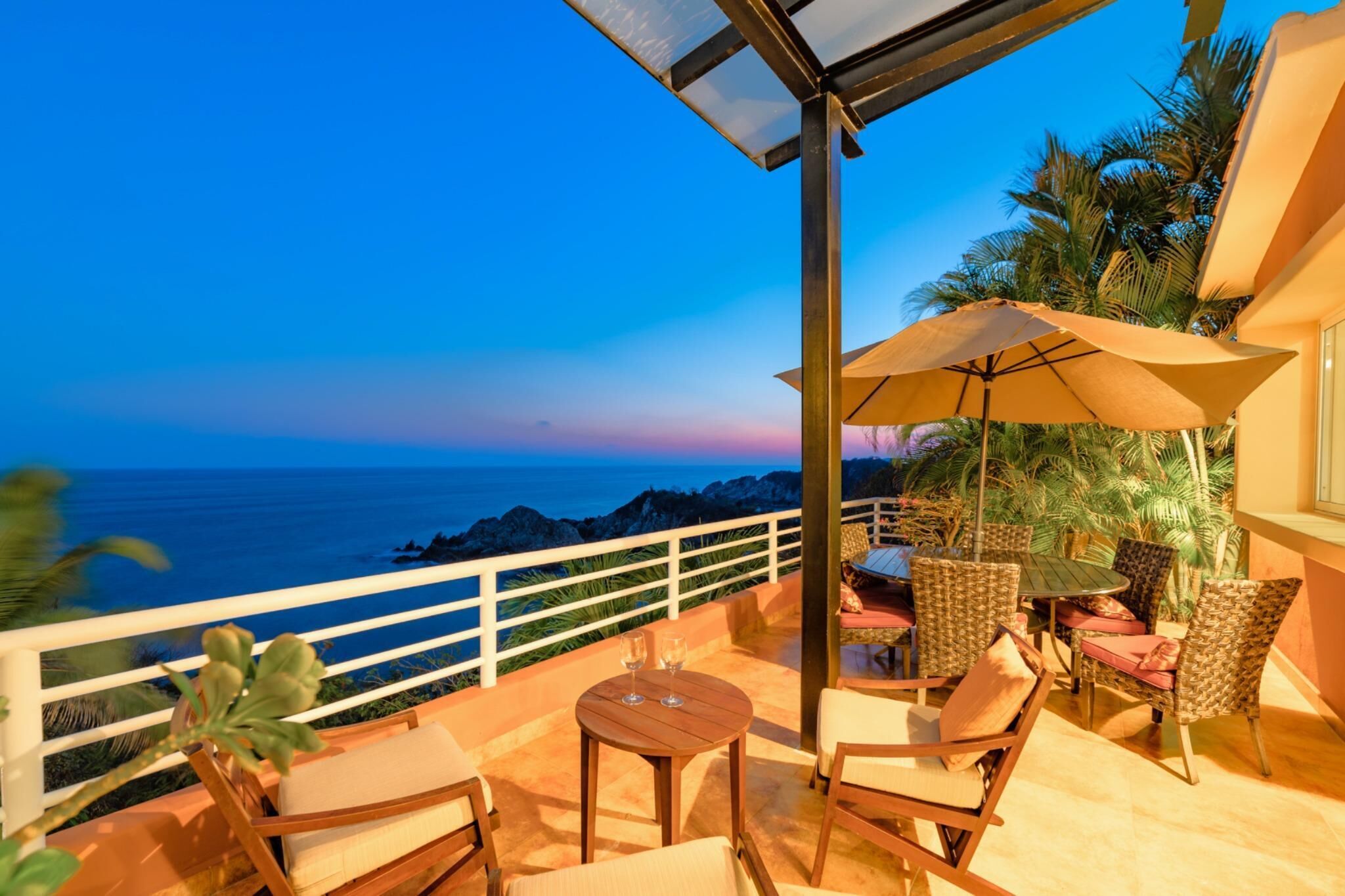 A balcony with a view of the ocean, furnished with chairs and a table, and a large umbrella.