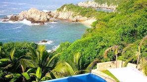 Vista costeira com piscina, falésias rochosas e vegetação exuberante.