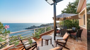 A balcony with a view of the ocean, furnished with chairs and a table, and a glass railing. - Villa Diamante (Santa María Huatulco)