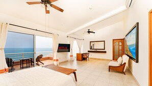 A spacious hotel room with a large bed, a balcony with a view of the ocean, a desk, and a TV. - Villa Diamante (Santa María Huatulco)