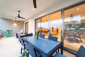 A modern dining area with a glass partition, wicker furniture, ceiling fans, and a view of the interior.