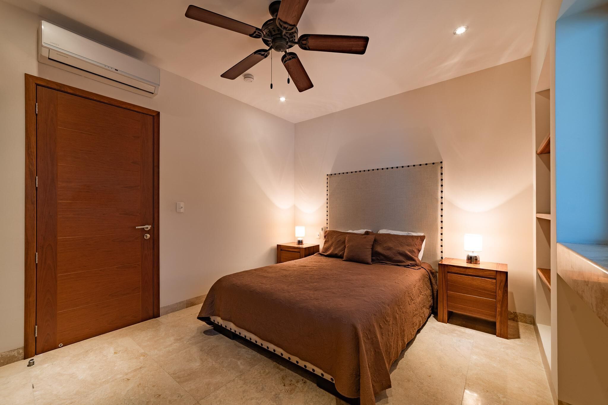 Een slaapkamer met een groot bed, een houten hoofdbord, twee nachtkastjes met lampen, een plafondventilator en een airconditioning.