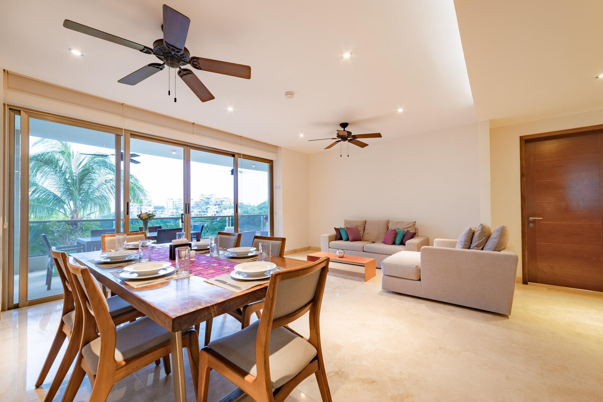 A spacious living area with a dining table set for four, a sofa, and two ceiling fans.
