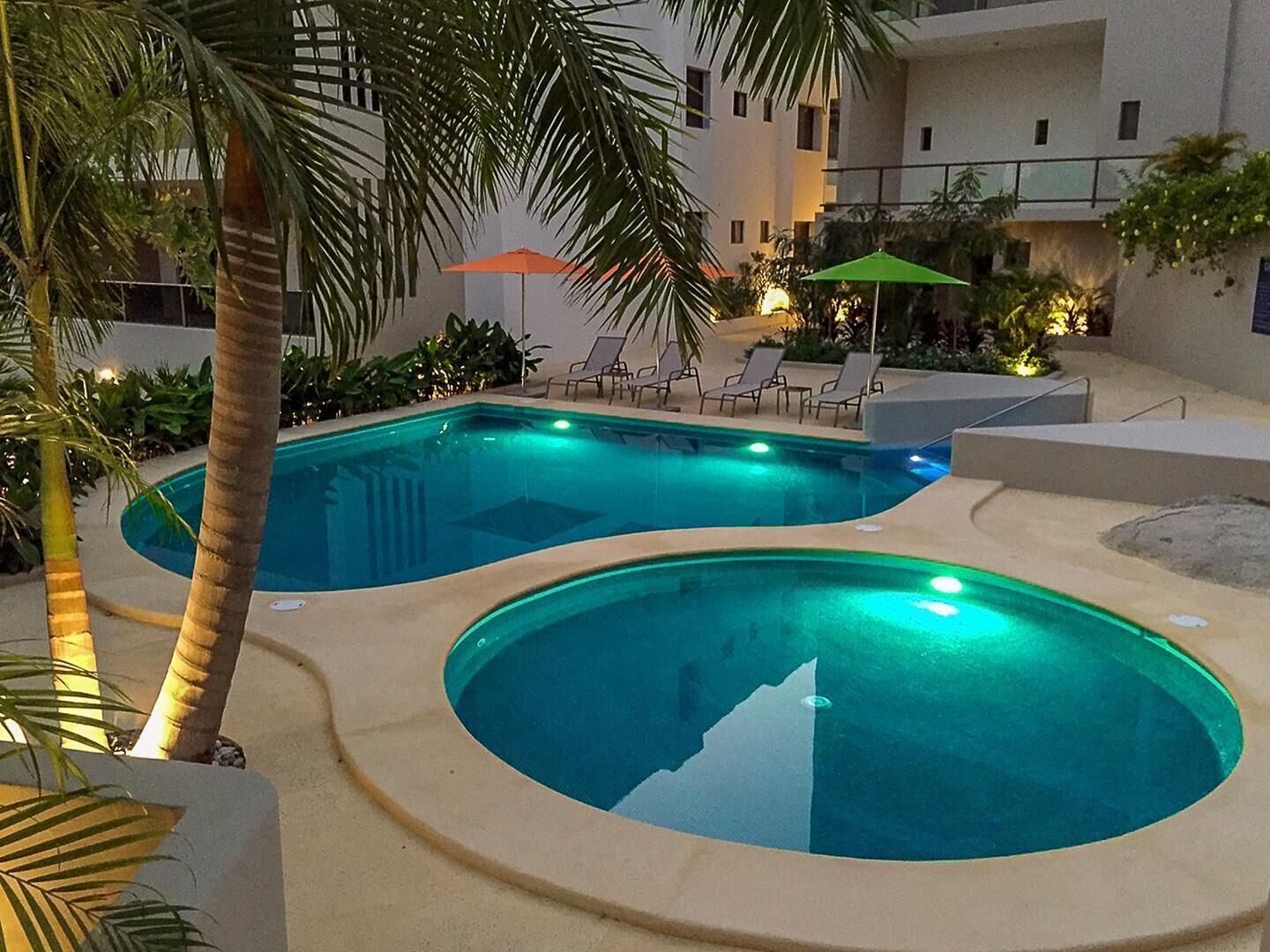 Una piscina con dos zonas separadas, rodeada de palmeras y sillas de descanso.