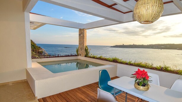 Un área de estar exterior moderna con piscina, terraza de madera y vistas al mar.