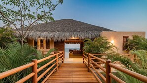 A wooden bridge leading to a thatched-roof building with a view of the sea. - Villa Alheli (Santa María Huatulco)