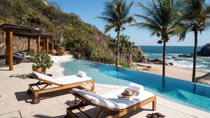 A poolside area with lounge chairs, a pergola, and a view of the ocean. - Villa Alheli (Santa María Huatulco)