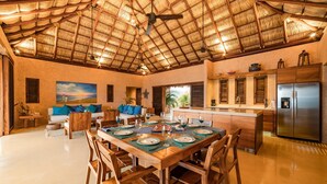 A spacious living area with a dining table set for six, a kitchen with modern appliances, and a thatched roof ceiling. - Villa Alheli (Santa María Huatulco)