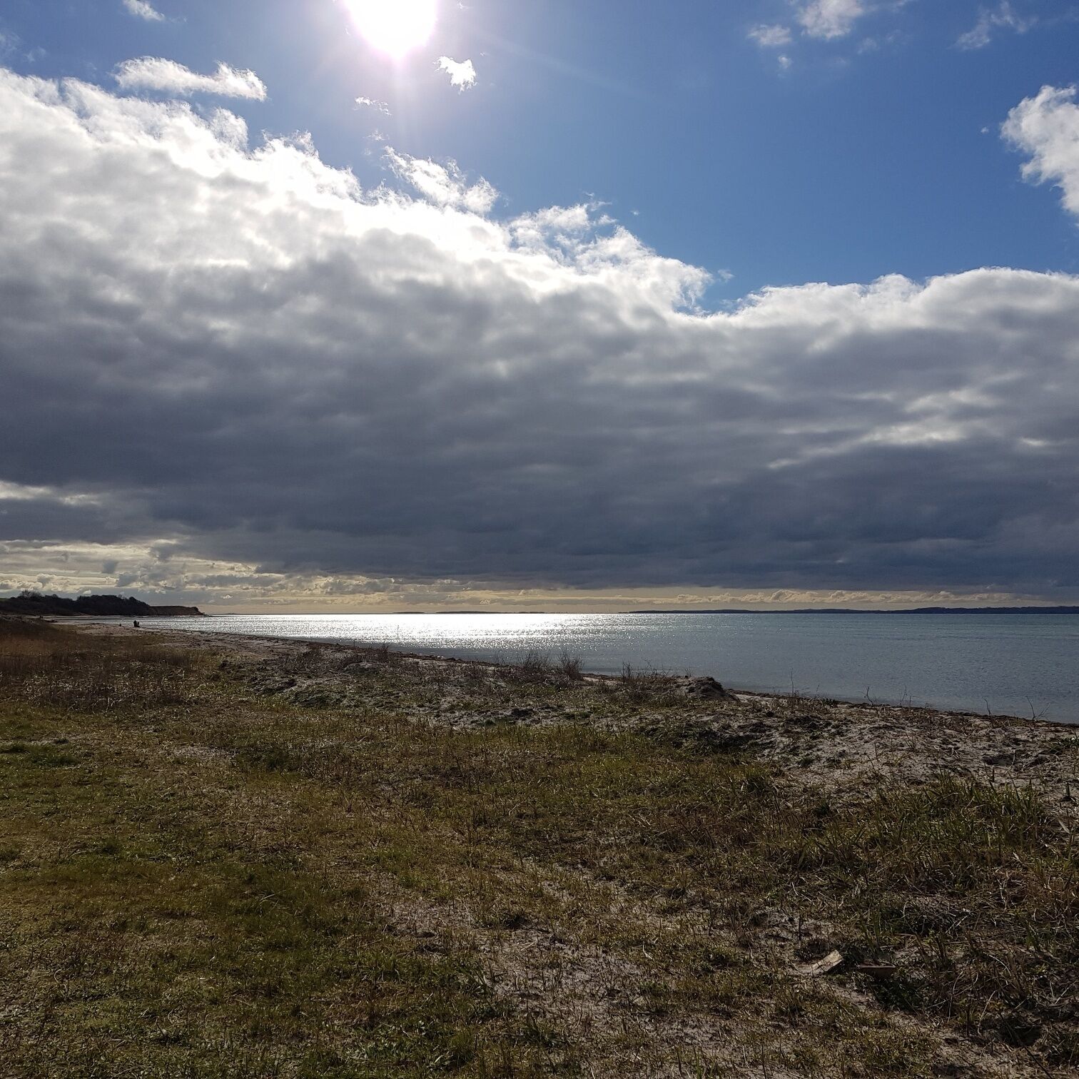 A beach with a clear view of the water and distant land under a partly cloudy sky.