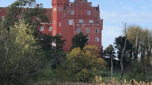 Ein großes, schlösserähnliches Gebäude in Rot mit zahlreichen Fenstern und einem Turm, umgeben von Bäumen und Grünflächen.