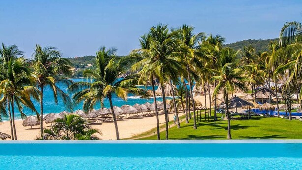 A poolside view with a clear blue pool, palm trees, and a beach in the background. - Villa Lu Iba (Santa María Huatulco)