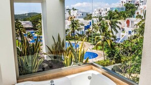 A modern bathroom with a large bathtub and a view of a resort with palm trees and a pool. - Villa Lu Iba (Santa María Huatulco)